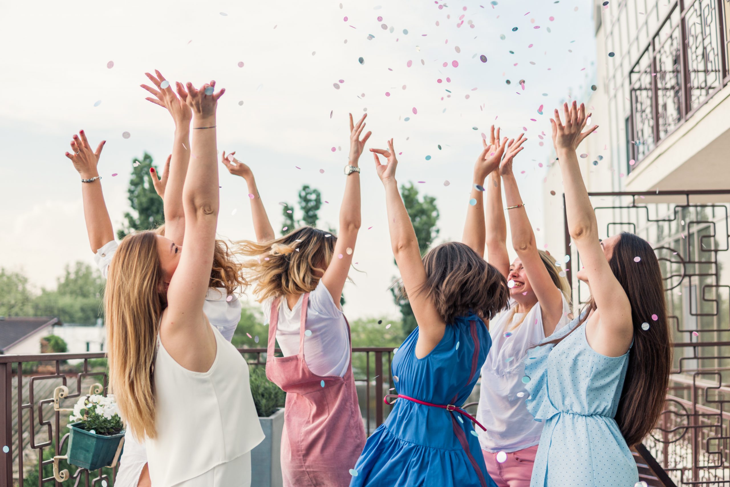 Girls Party. Beautiful Women Friends on the balcony Having Fun At Bachelorette Party. They are dancing in confetti with hands up